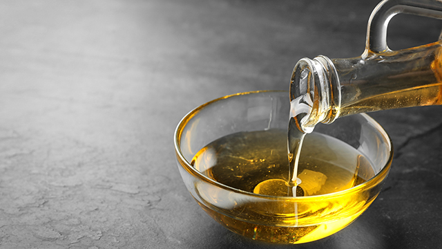 Pouring cooking oil from jug into bowl on black table